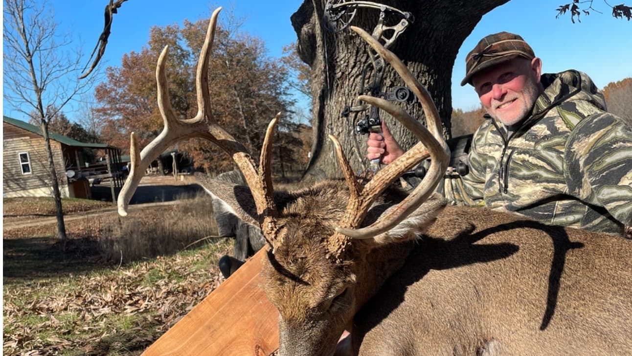 Hunter with impressive buck antlers and bow in camouflage.