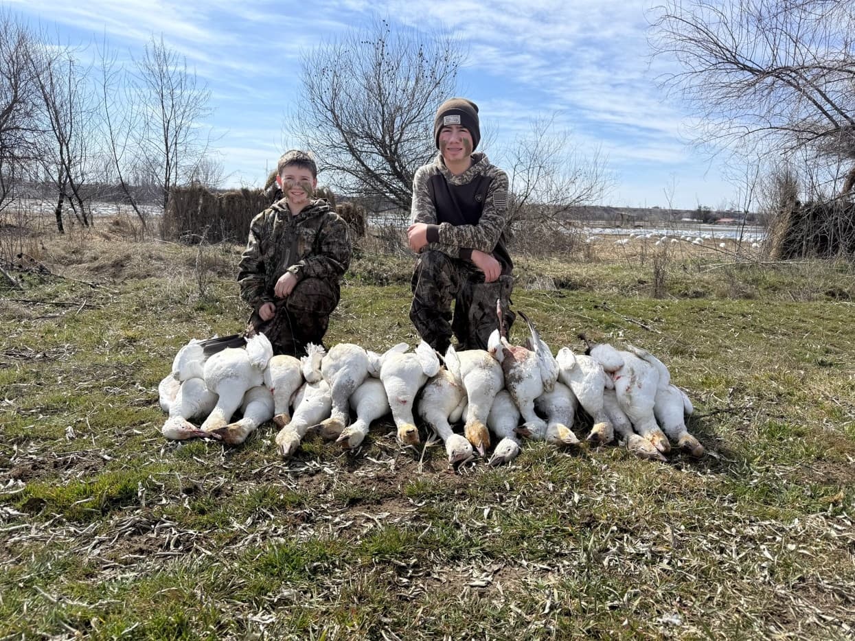 Two boys in camouflage pose with a pile of dead snow geese.