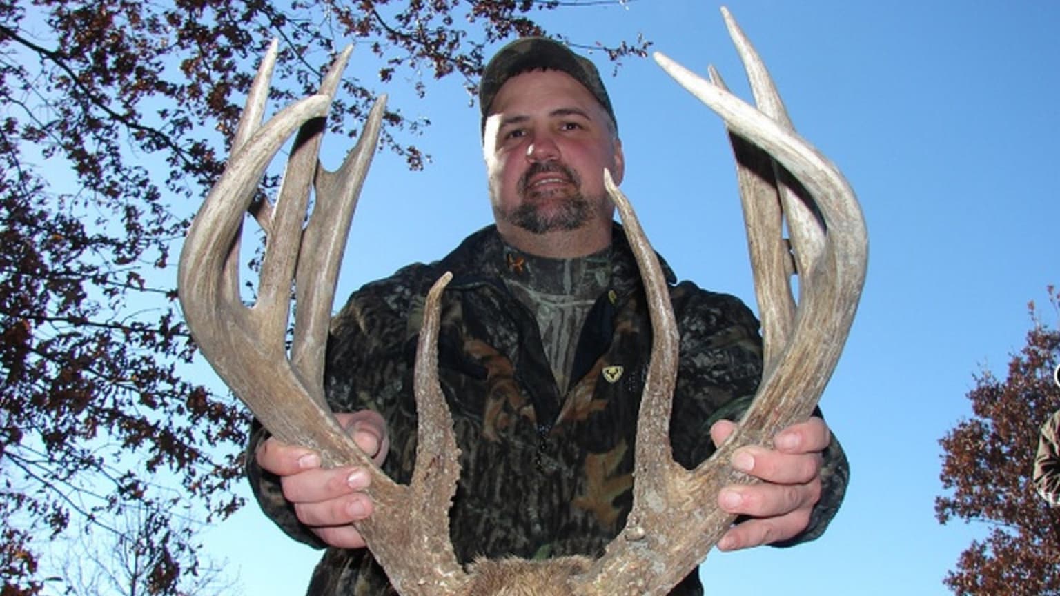 Man in camouflage holding large deer antlers.