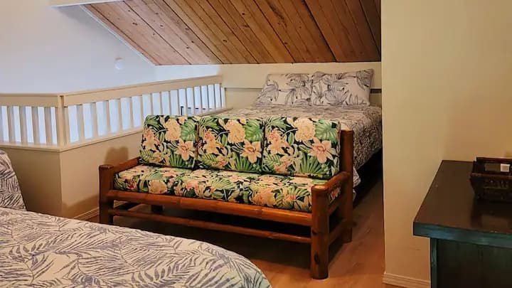 Loft bedroom with wooden ceiling and railing. Floral print sofa and bed with matching pillows. Wooden furniture throughout.