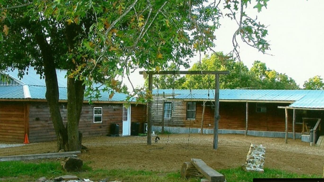 Rustic wooden buildings with teal roofs and a wooden swing set in the yard.