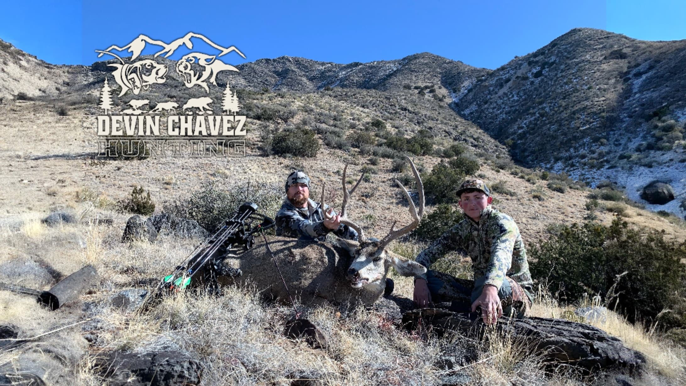 Two hunters pose with a harvested buck in a mountainous terrain. Bow and arrows lie nearby. A hunting logo overlays the top.