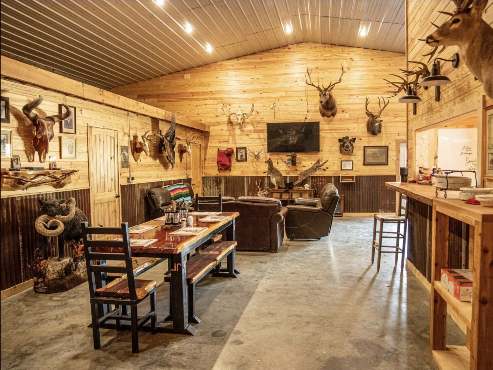 Rustic room with mounted animal heads, a dining table, seating area, and a bar.