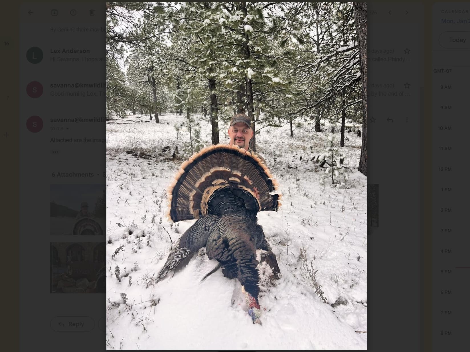 Man holding a dead turkey in snow-covered forest. The turkey's tail feathers are fanned out, and the man smiles. Snowy tre...