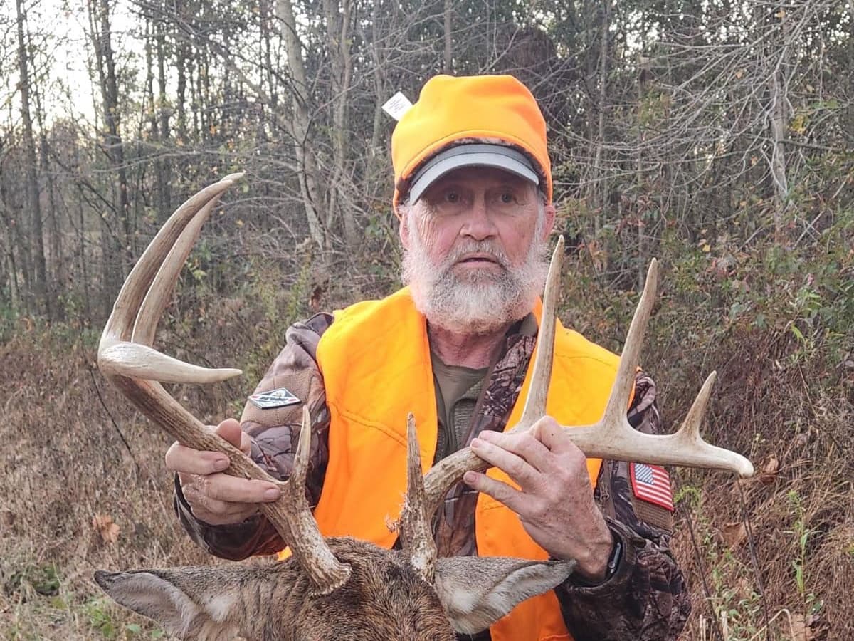Hunter in orange vest and hat holds large deer antlers.