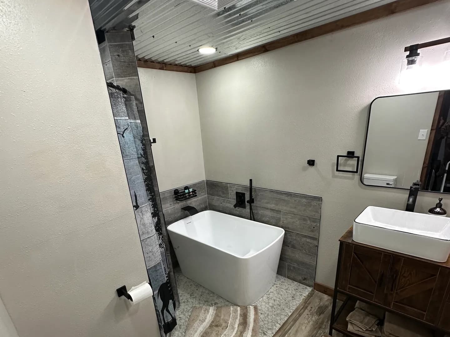Modern bathroom with a white freestanding tub, wood-look vanity with rectangular sink, and gray tiled accent wall.