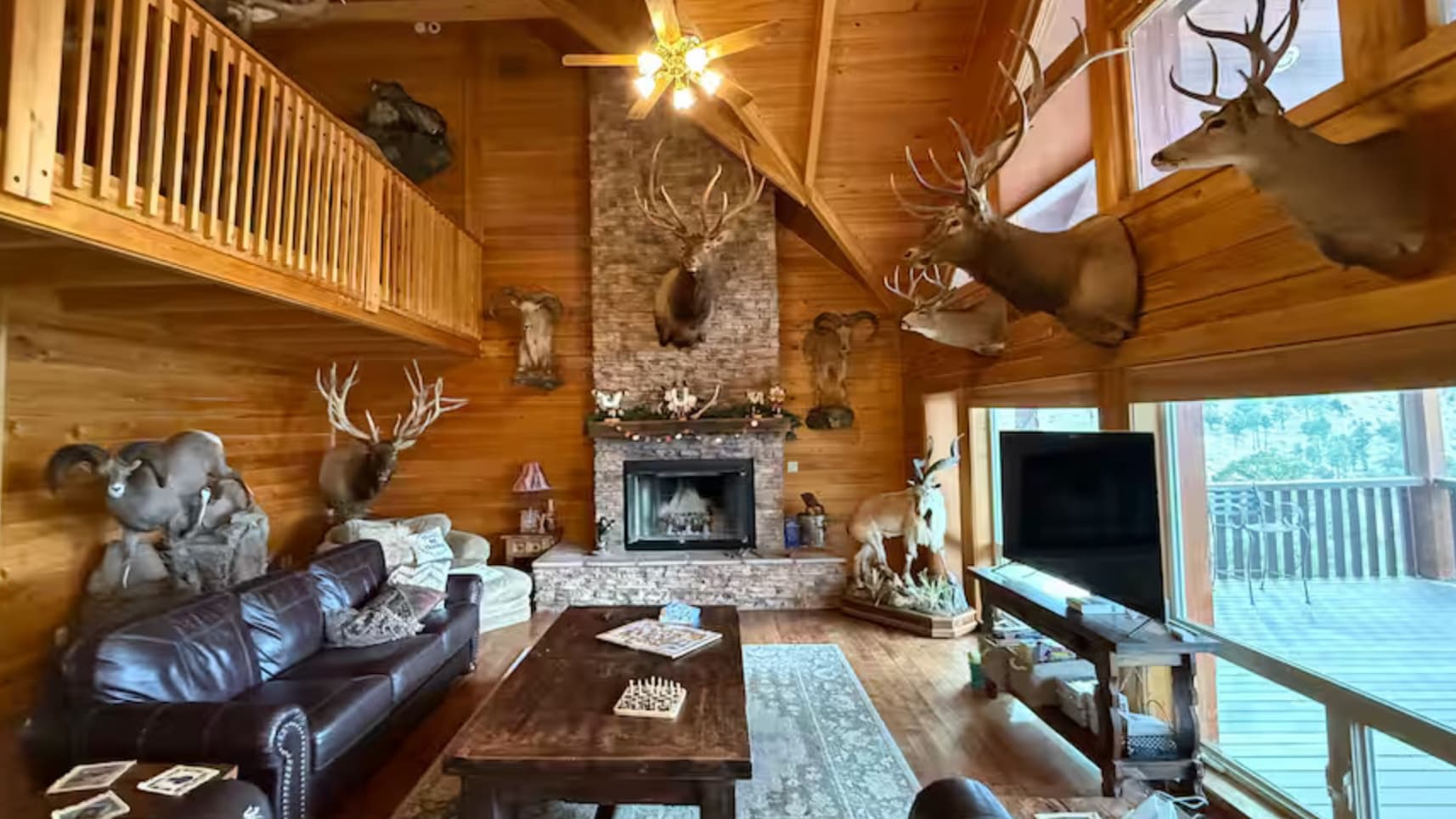 Lodge interior with wood paneling, multiple deer and elk trophy mounts, a fireplace, and a leather sofa. The ceiling featu...