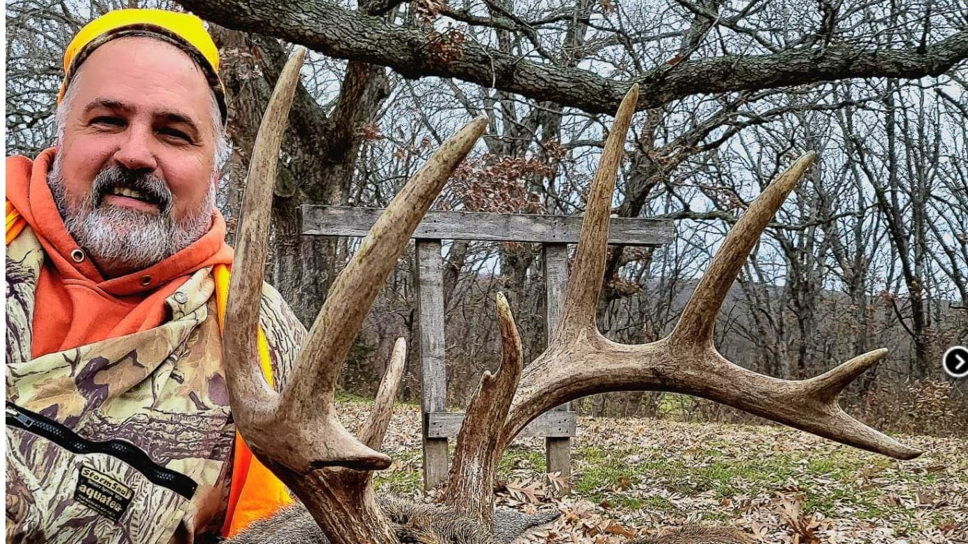 Man in orange hunting gear with a large rack of deer antlers.