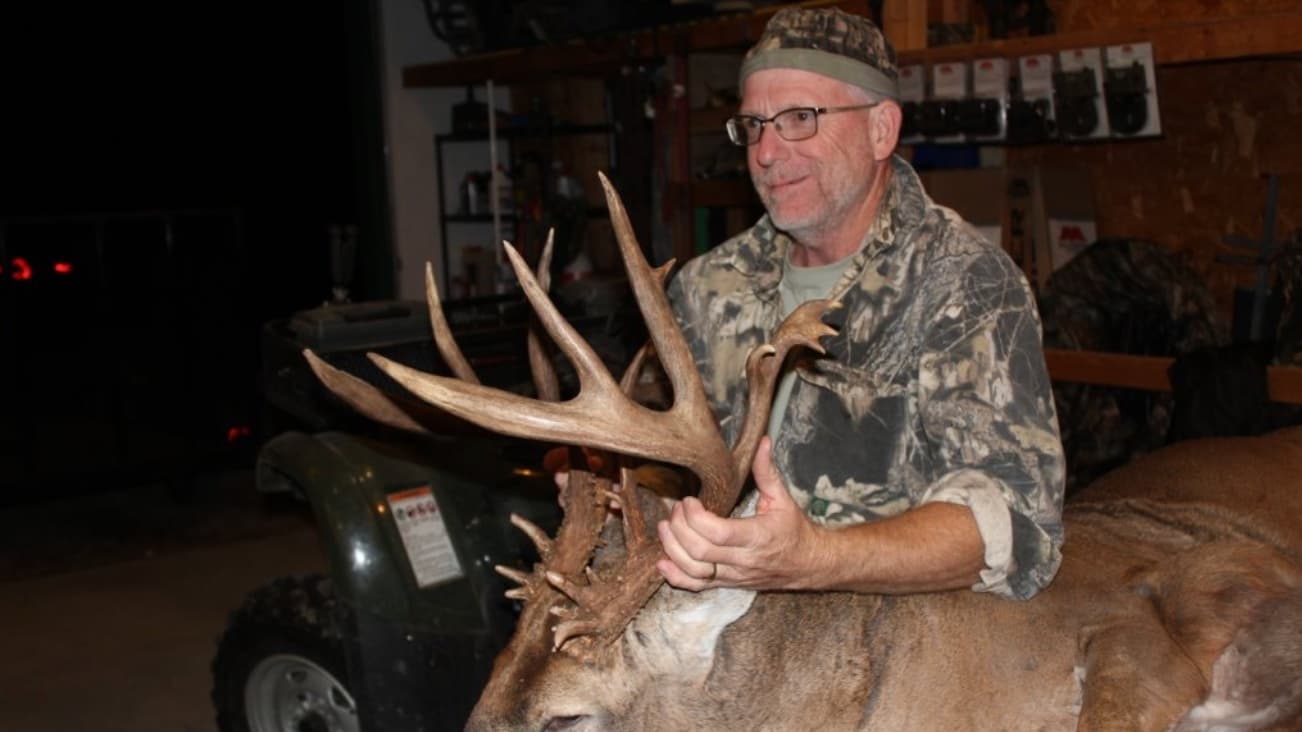 Hunter with large deer antlers; ATV in background.