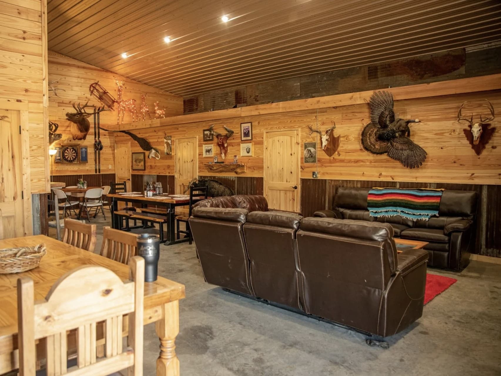 Taxidermied animals adorn wood-paneled walls of a rustic room with leather couches and dining tables.