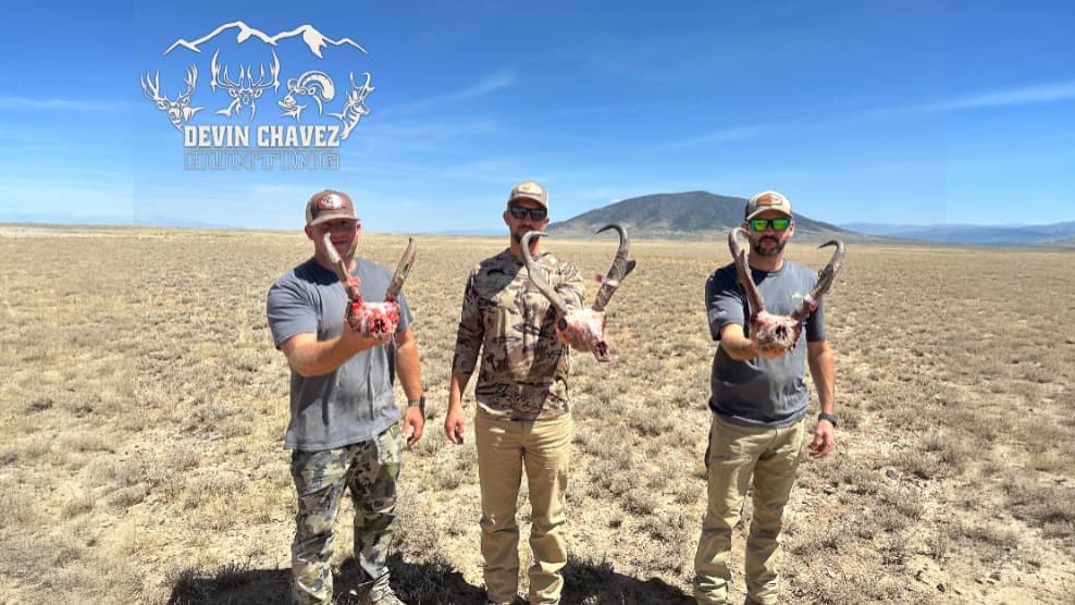 Three men in hats holding animal skulls with antlers, standing in a field. Logo above reads "Devin Chavez Hunting."