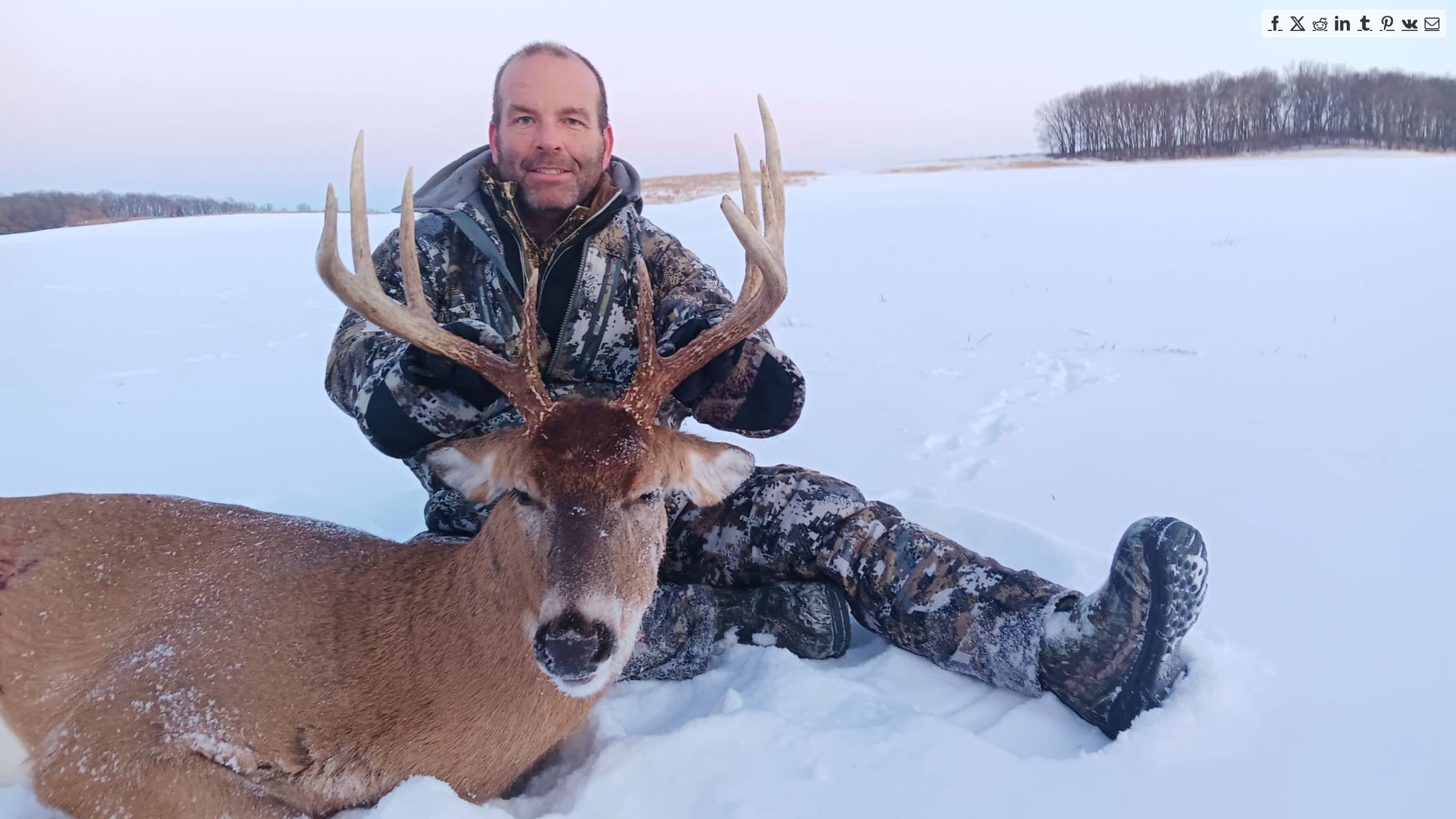 Hunter sits in snow holding large antlered deer.