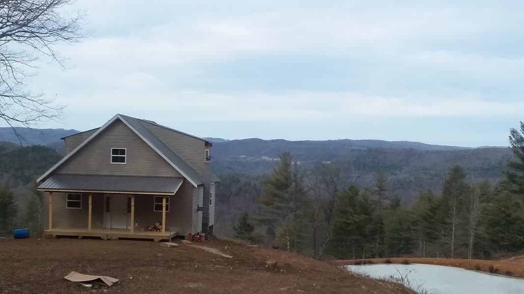 New construction house on a hillside with a porch, overlooking a wooded valley and rolling hills.