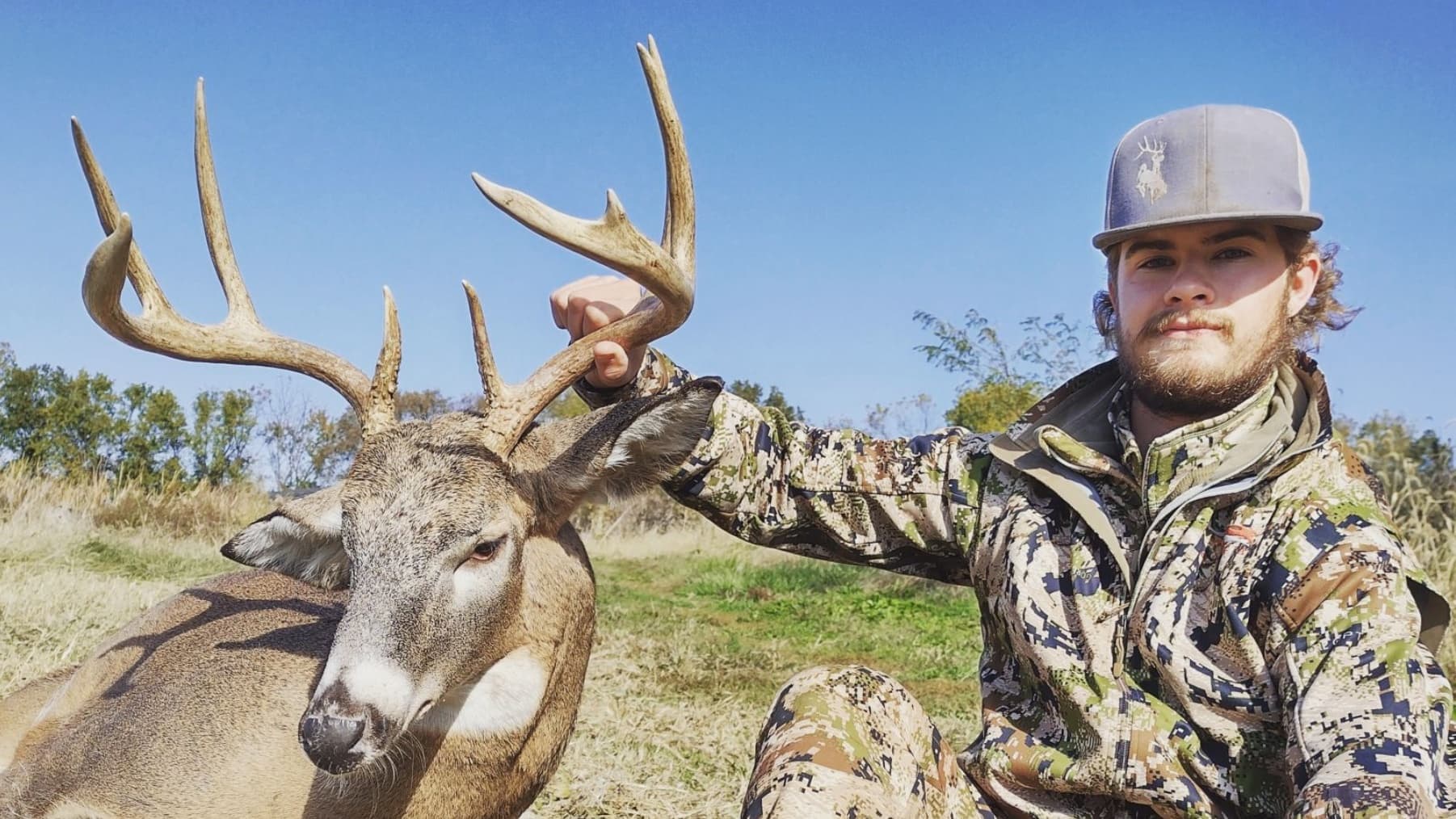 Young hunter with large-antlered deer in field.